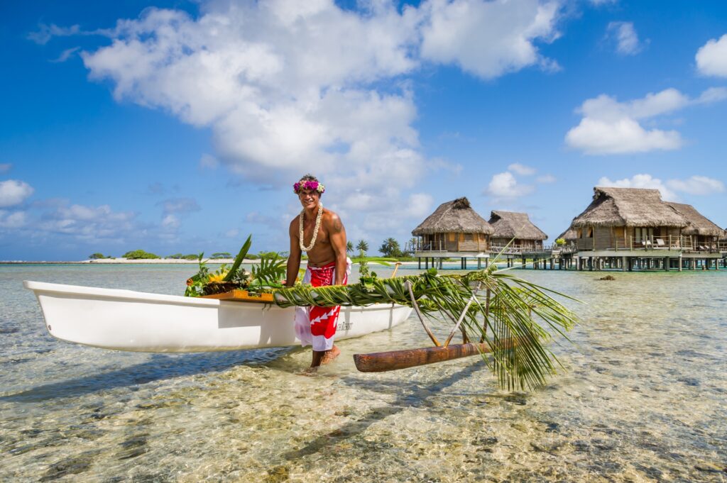 Un hombre llevando un canoa por polinesia en la playa con WAYAO